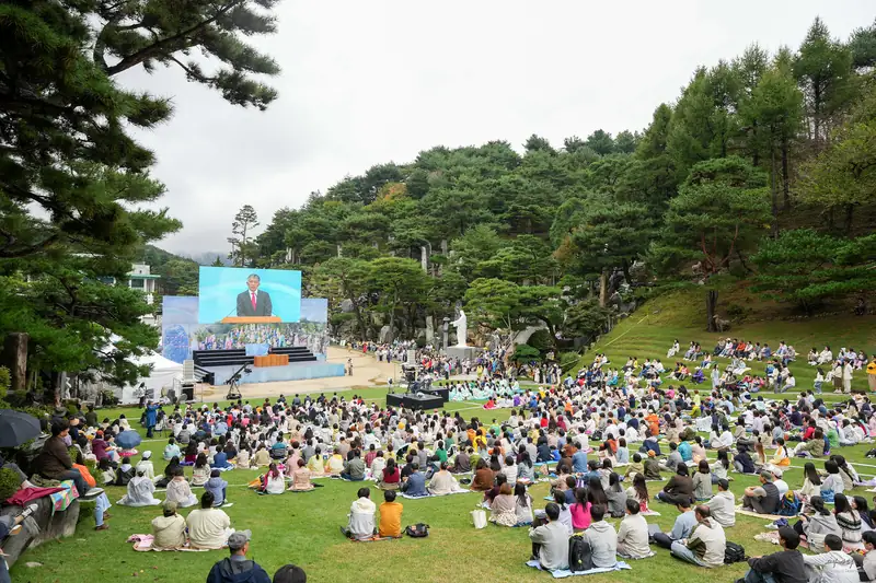 잔디밭에 모여 앉아 대형 화면으로 말씀을 듣는 참가자들